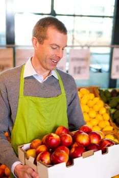 A happy male grocer with a box of ripe peaches