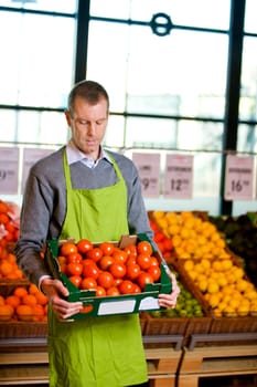 A male grocery owner with a box of ripe tomatoes