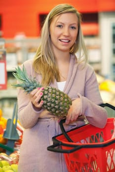 Cheerful young woman holding pineapple with basket in the supermarket