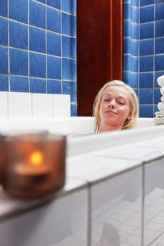 Beautiful young woman in bathtub at luxury spa with candle in glass