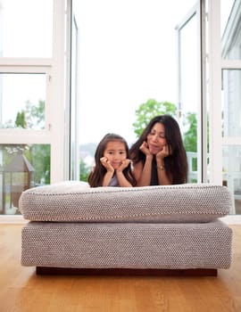 Happy mother and daughter sitting on a couch cushion with a smile, mother looking lovingly at daughter