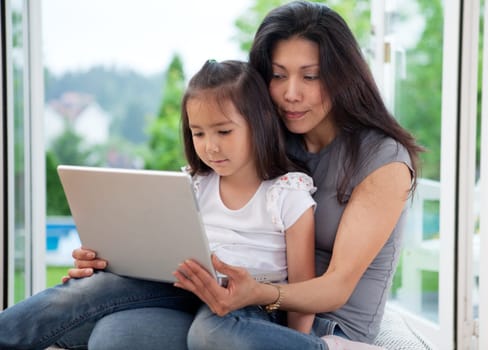 Cute young daughter together with mother using a laptop in a house interior