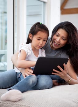 A cute happy mother and daughter using a digital tablet at home in the living room