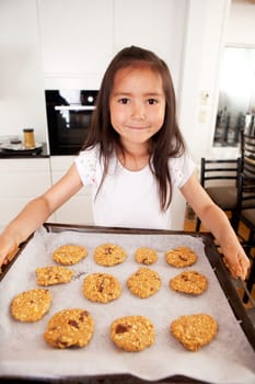 Cute young girl looking at camera with bakng sheet full of raw cookies
