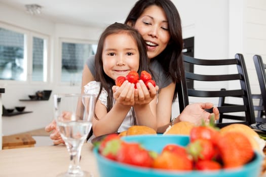 Mother and daughter sitting at table in kitchen with handful of strawberries