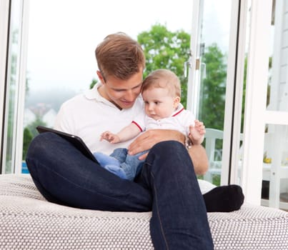 Father and son sitting in front of window using a digital tablet
