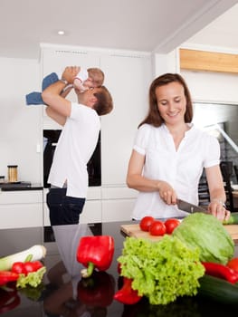 Happy family at home with mother making salad and father playing with son in background