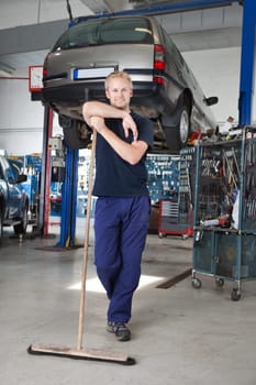 Full length portrait of young man leaning on broom in garage