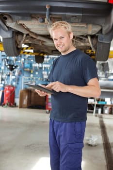 Portrait of young mechanic standing and using digital tablet in his auto repair shop