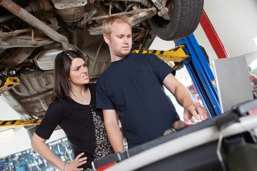 Irritated young woman standing with mechanic using laptop in garage