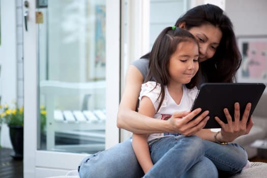 Mother and Daughter having fun on a digital tablet in a home interior