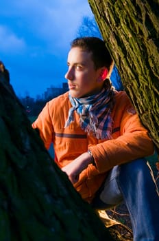 Three-quarter portrait of a young male teenager sitting at one and looking to the side at dusk