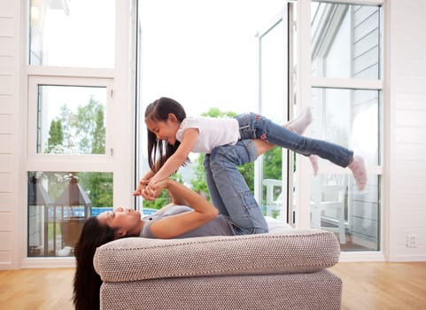 Playful mother giving daughter an airplane ride with arms and feet