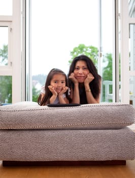 Portrait of a mother and daughter in home interior looking at the camera with their heads leaning on hands