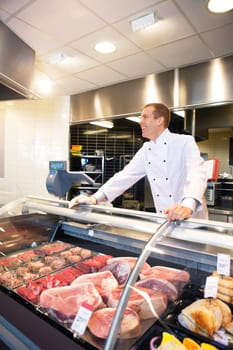 Cheerful chef on the counter of frozen meat in the supermarket
