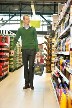 Mid adult man with shopping basket walking in grocery store and looking at products