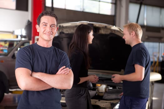 Portrait of a mechanic looking at the camera with a customer and second mechanic in the background