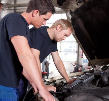 Two man mechanics looking a diagnostics equipment, servicing car