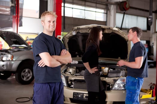 Mechanic looking at camera with customer and second mechanic in background