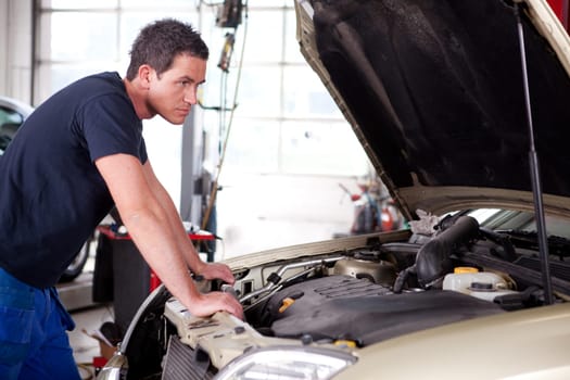 A young mechanic staring at a car, thinking