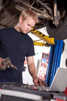 An automechanic referring to a laptop for the service order or manual
