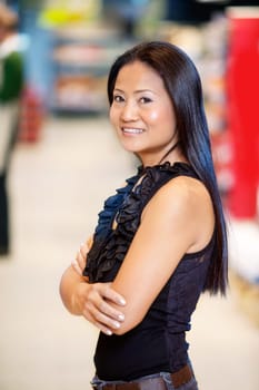 Confident smiling asian woman with arms crossed in shopping centre looking at camera