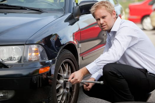 An unhappy business man changing a tire on the road