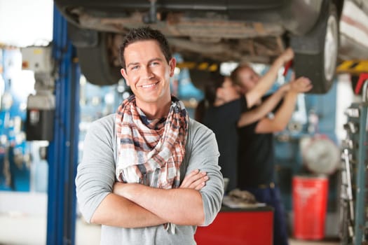 Portrait of a male happy customer in an auto repair shop with mechanics in background