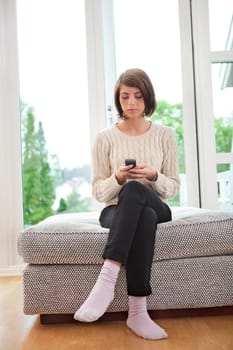 Young attractive woman text messaging while sitting on couch