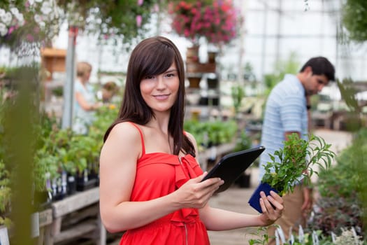 Beautiful woman holding tablet pc and potted plant with people in background