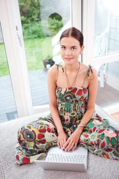 Portrait of a smiling young woman using a laptop while sitting on couch