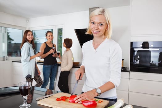 Portrait of happy female cutting vegetables while friends having drink in background