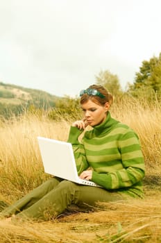 Young business woman working on laptop computer on golden meadow at mountains outdoors