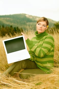 Young business woman holding laptop computer on golden meadow at mountains outdoors