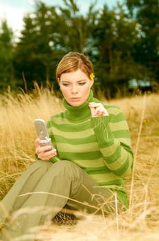 Young business woman using cell phone on golden meadow at mountains outdoors