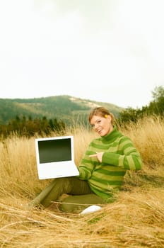 Young business woman holding laptop computer on golden meadow at mountains outdoors