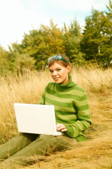 Young business woman working on laptop computer on golden meadow at mountains outdoors