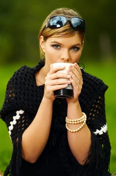 Young business woman with cup during picnic on green meadows outdoors