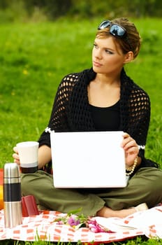 Young business woman working on laptop computer during picnic on green meadows outdoors