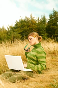 Young business woman working on laptop computer on golden meadow at mountains outdoors