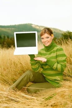 Young business woman holding laptop computer on golden meadow at mountains outdoors