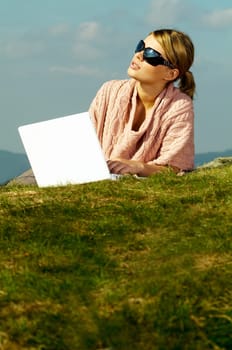 Young business woman relaxing, working on laptop computer on meadow