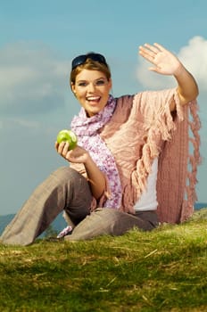 Young business woman relaxing on meadow, holding green fresh apple