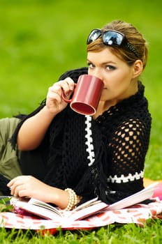 Young business woman with cup during picnic on green meadows outdoors