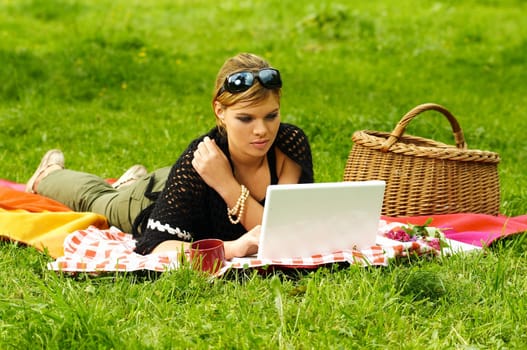 Young business woman working on laptop computer during picnic on green meadows outdoors