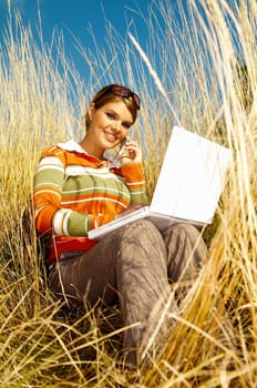 Young business woman relaxing, working on laptop computer and talking cell phone on meadow