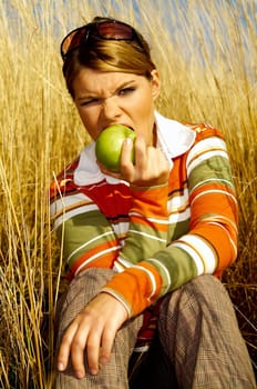Young business woman relaxing on meadow, holding green fresh apple