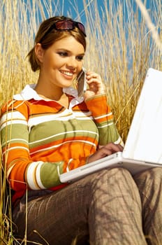 Young business woman relaxing, working on laptop computer and talking cell phone on meadow