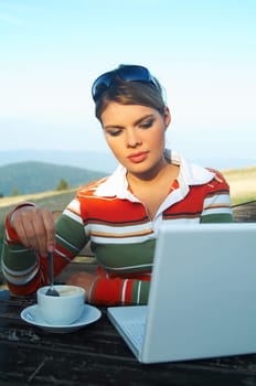 Young woman relaxing, drinking coffee, working on laptop computer on mouintain outdoors