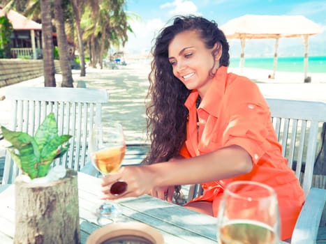 Young woman with glass of wine has a dinner on the beach